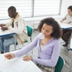 Grupo de estudantes faz uma prova em uma sala de aula iluminada.