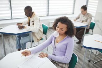 Grupo de estudantes faz uma prova em uma sala de aula iluminada.