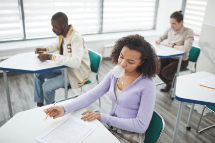 Grupo de estudantes faz uma prova em uma sala de aula iluminada.