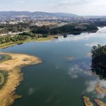 Vista aérea de um reservatório brasileiro, com área urbana ao fundo.