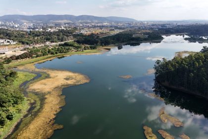 Vista aérea de um reservatório brasileiro, com área urbana ao fundo.