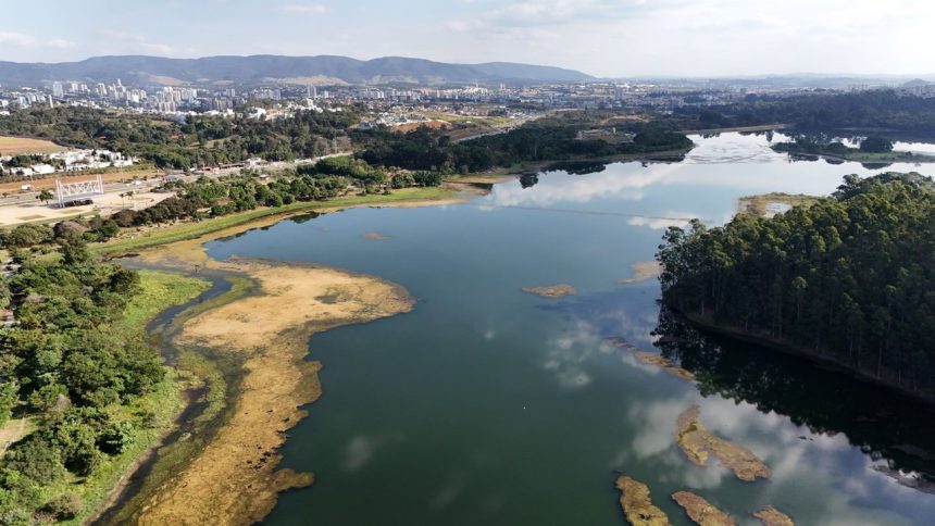 Vista aérea de um reservatório brasileiro, com área urbana ao fundo.