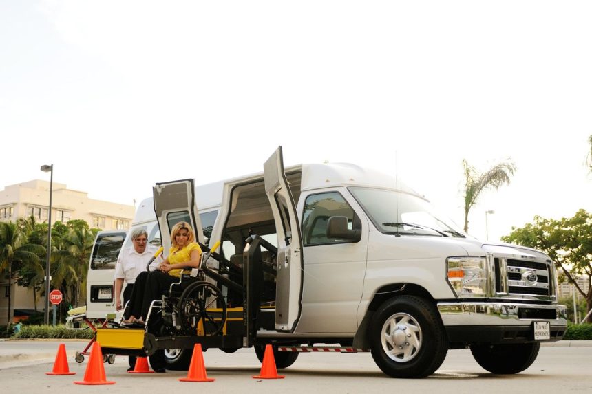 Mulher em cadeira de rodas embarca em uma van acessível por meio de uma plataforma elevatória, com auxílio de um motorista.