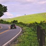 Carro trafega por uma estrada sinuosa em meio à paisagem rural brasileira.