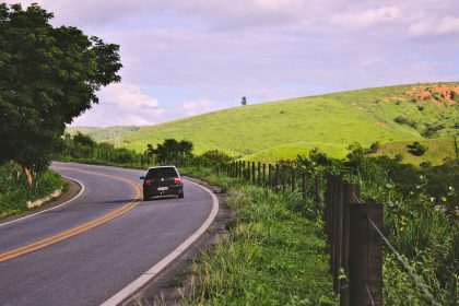 Carro trafega por uma estrada sinuosa em meio à paisagem rural brasileira.