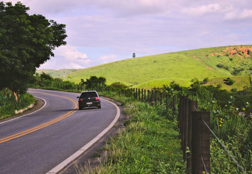 Carro trafega por uma estrada sinuosa em meio à paisagem rural brasileira.