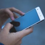 Mãos segurando e utilizando um smartphone, sem texto legível na tela.